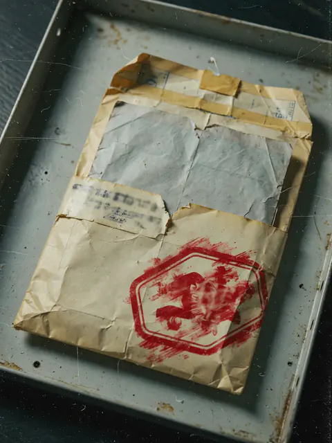 A worn, taped envelope in a steel tray, stamped with a red octagonal mark.